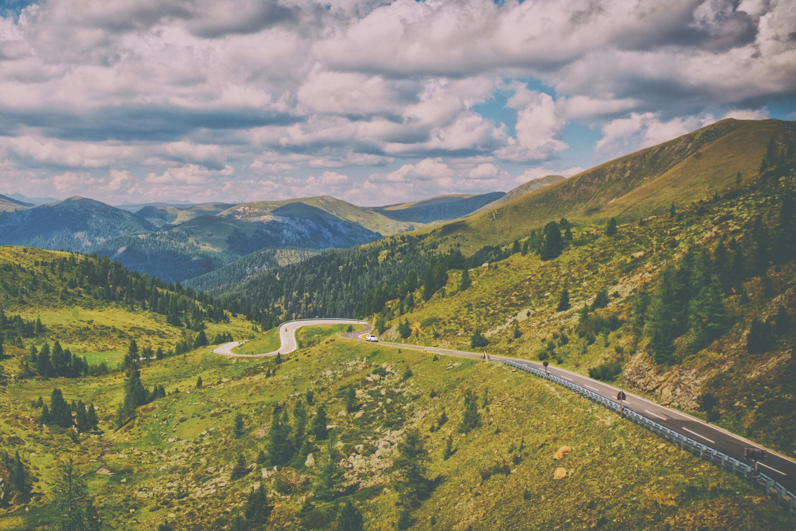 Captivating view of a mountain road winding through lush greenery under a vibrant sky.
